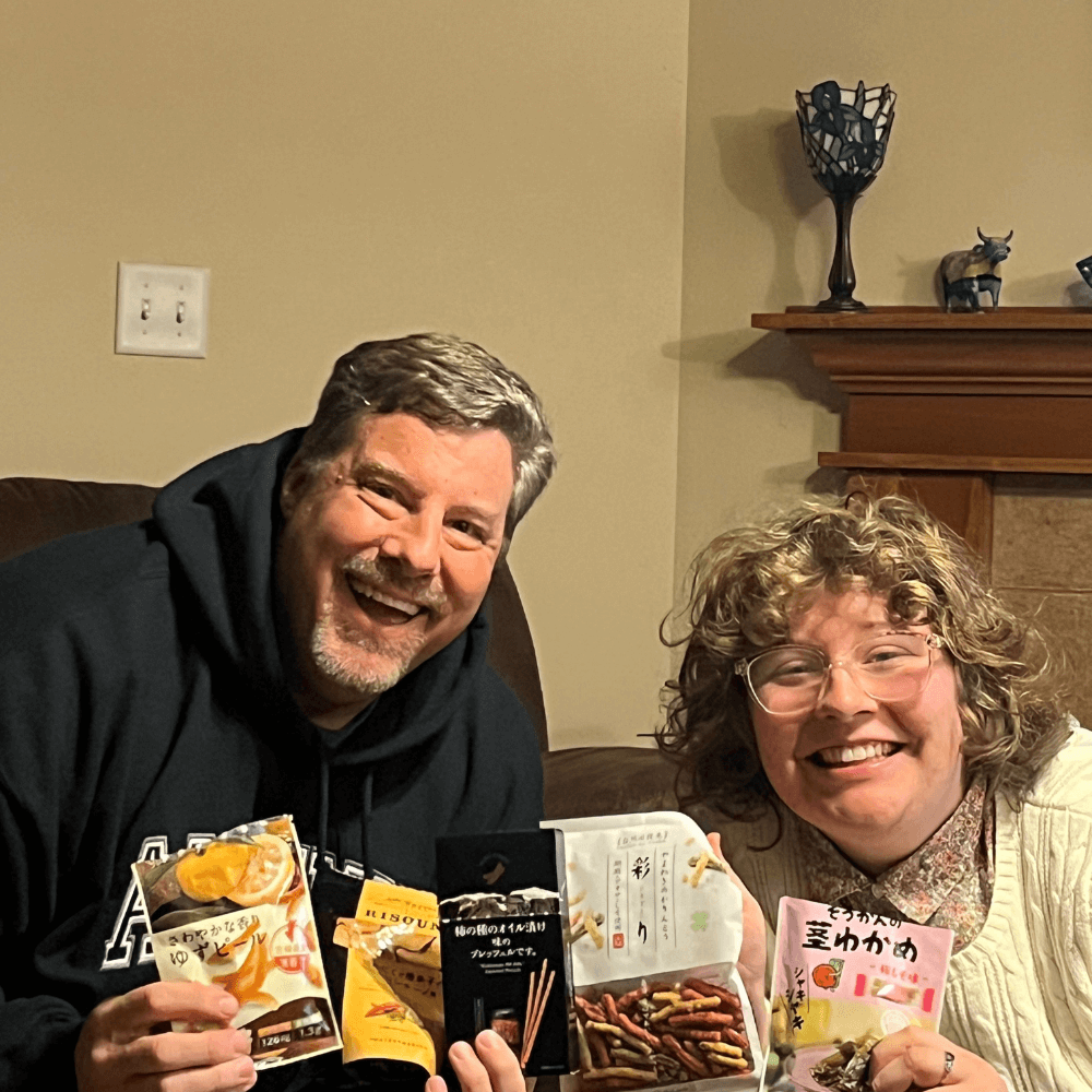 Two people sitting on a couch with authentic Japanese snacks in their hands.