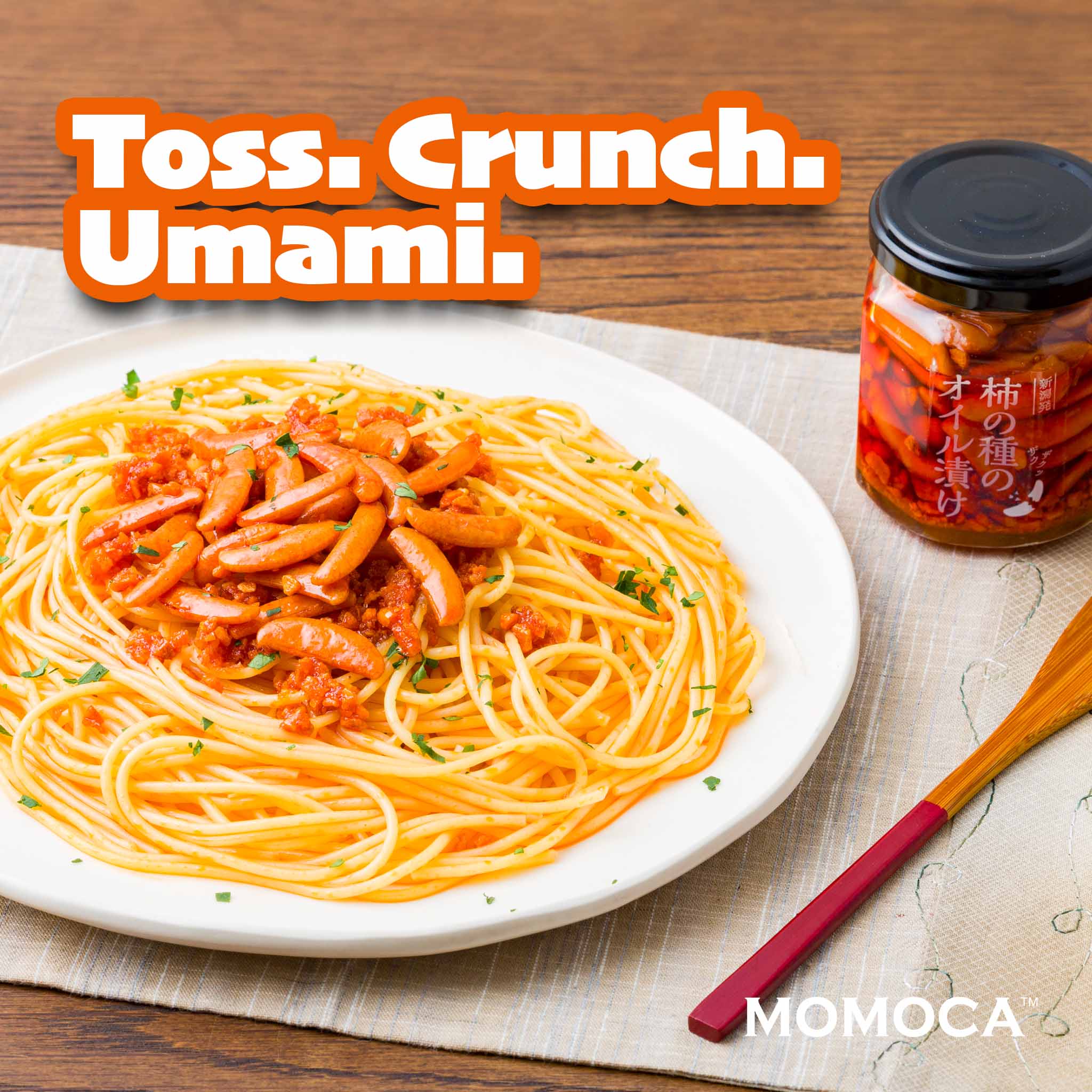 Spaghetti dish with a jar of sauce on a wooden table, featuring the text 'Toss. Crunch. Umami.' and 'MOMOCA'.