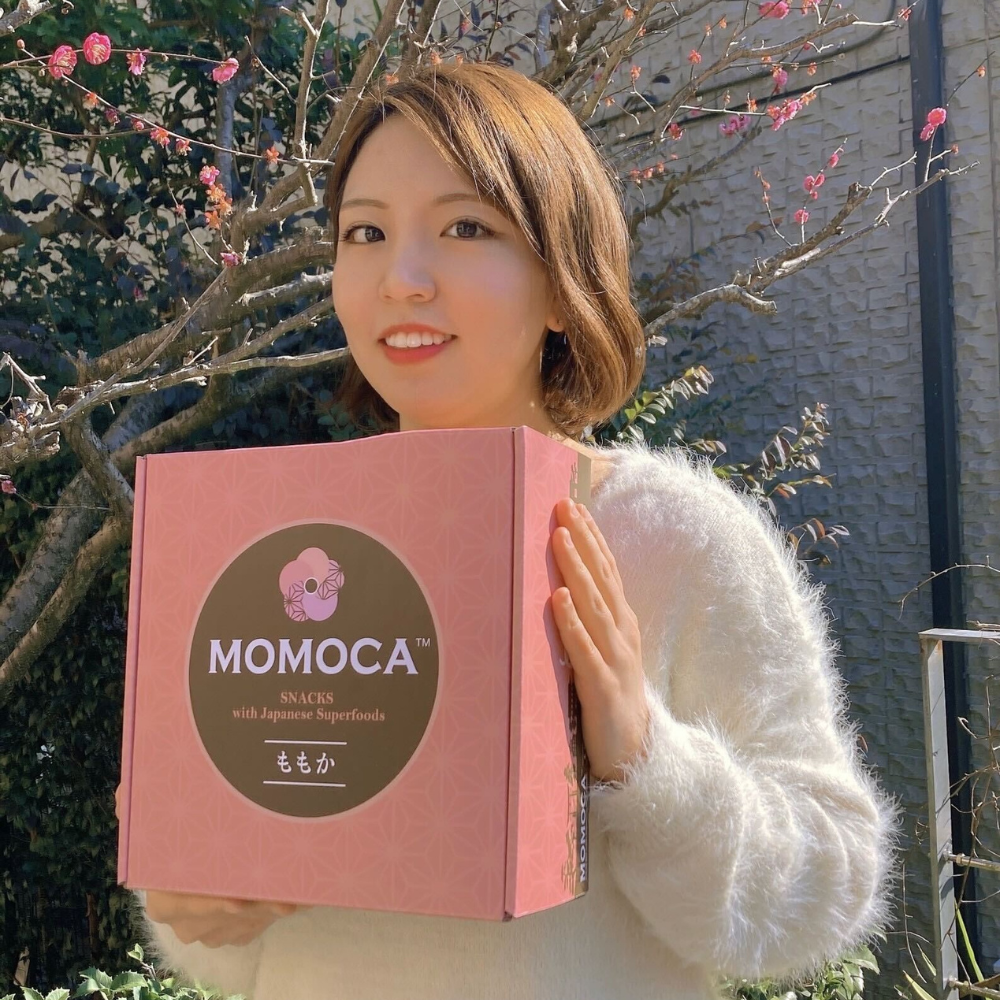 A woman holding up an authentic Japanese snacks box with the word Monica on it.