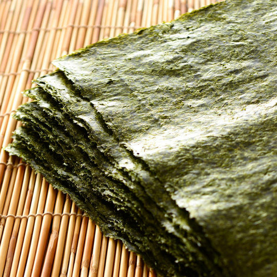 A stack of authentic Japanese snacks on a bamboo mat, including green seaweed.