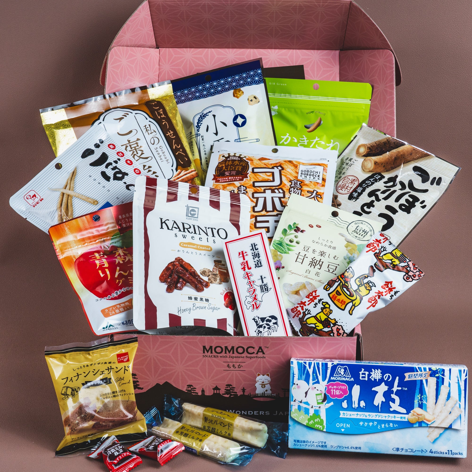 The Snow Flower Japanese Snack Box by MOMOCA showcases a variety of snacks elegantly presented in an open pink box.