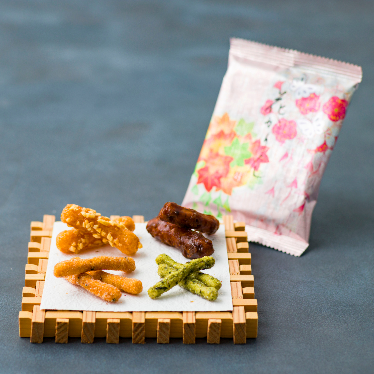 Assorted snacks on a wooden tray with a floral-patterned bag in the background.